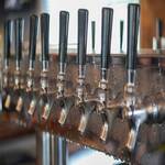 A row of beer taps with black handles is mounted on a metal draft system at a bar or brewery.